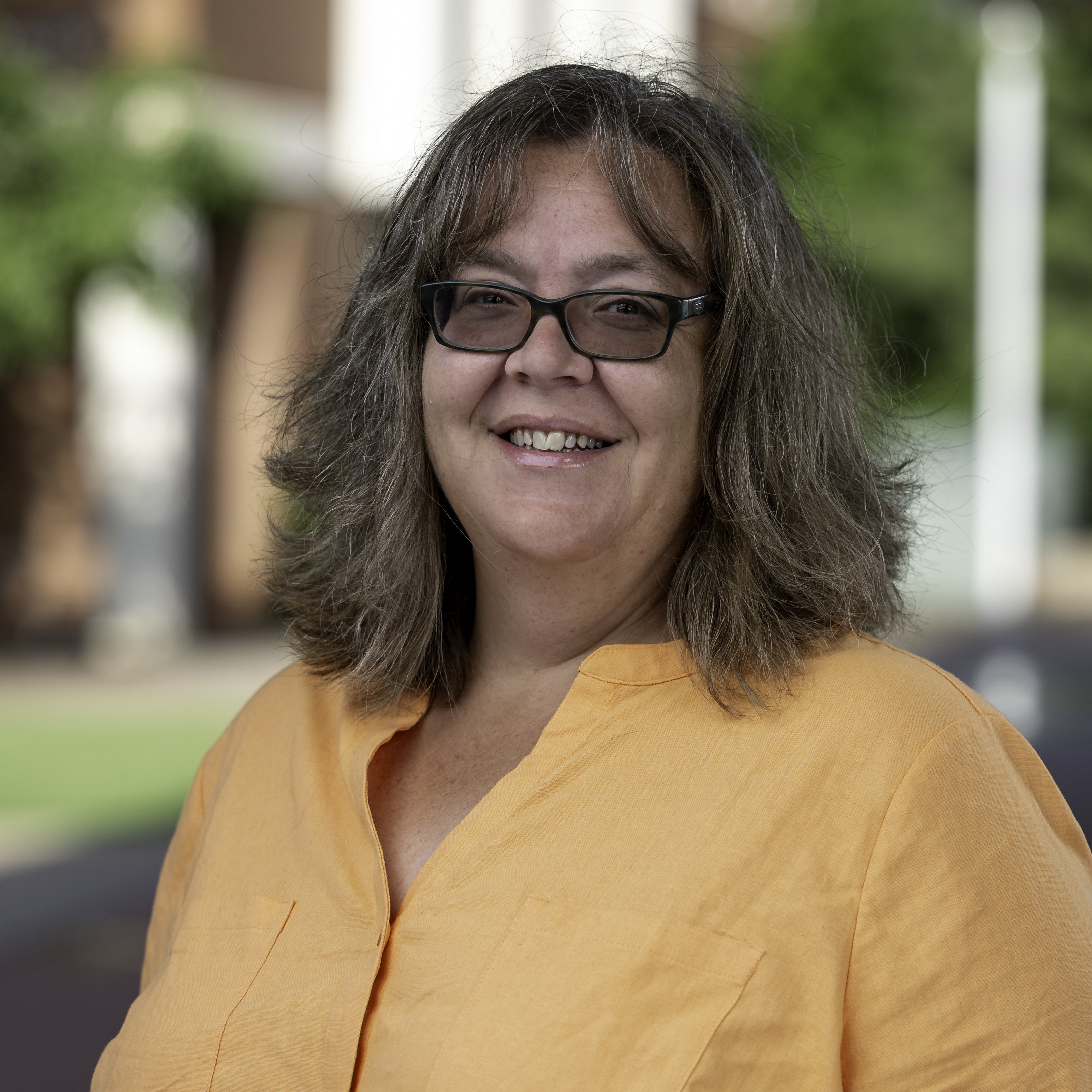 A headshot of Brandi Simmons, a woman with glasses and a yellow shirt. 
